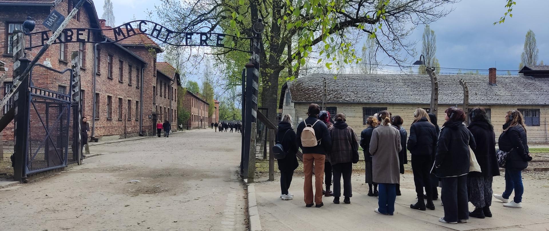 Wejście na teren byłego obozu koncentracyjnego Auschwitz, brama z napisem "Arbeit macht frei", przed bramą grupa zwiedzających