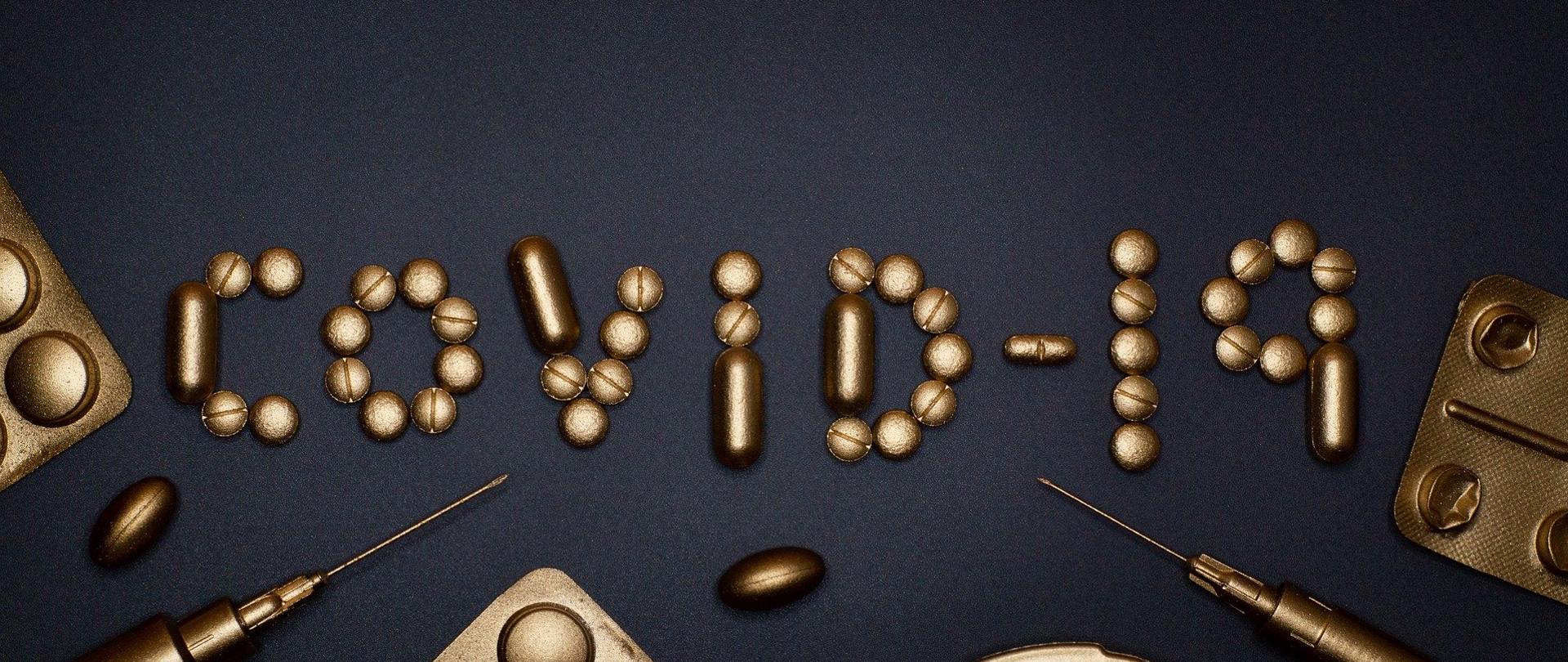 złote tabletki na czarnym tle ułożone w napis COVID-19.