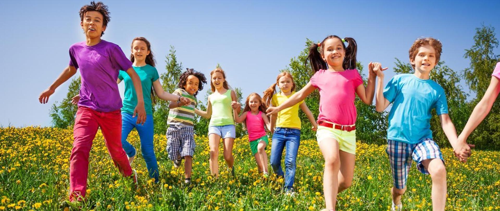 ośmioro uśmiechniętych dzieci biegnących po kwiecistej łące i trzymające się za ręce