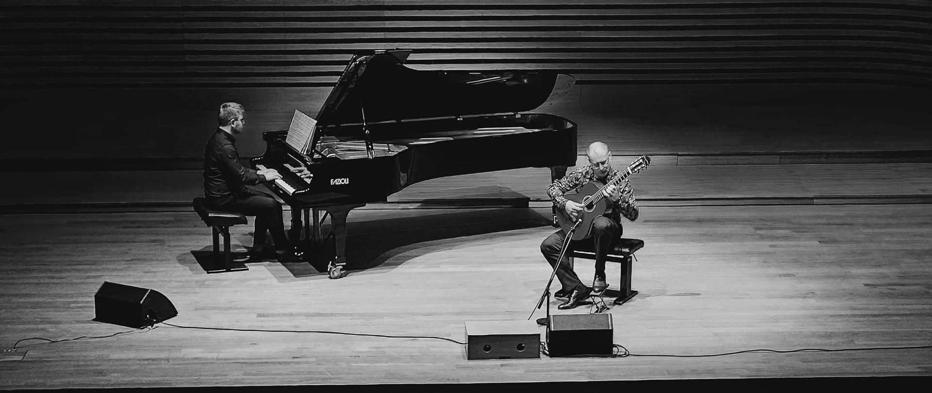 na scenie muzycy Andrzej Otremba grający na gitarze i Jakub Stachura grający na fortepianie. Zdjęcie czarno białe.