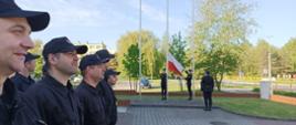 Na zdjęciu znajdują się strażacy dwóch zmian służbowych KP PSP w Wałczu ustawienie w dwuszeregu. W tle poczet flagowy wciąga flagę na maszt.