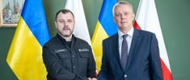 Ministers Tomasz Siemoniak and Ihor Klymenko stand on Polish-Ukrainian flags and shake hands.