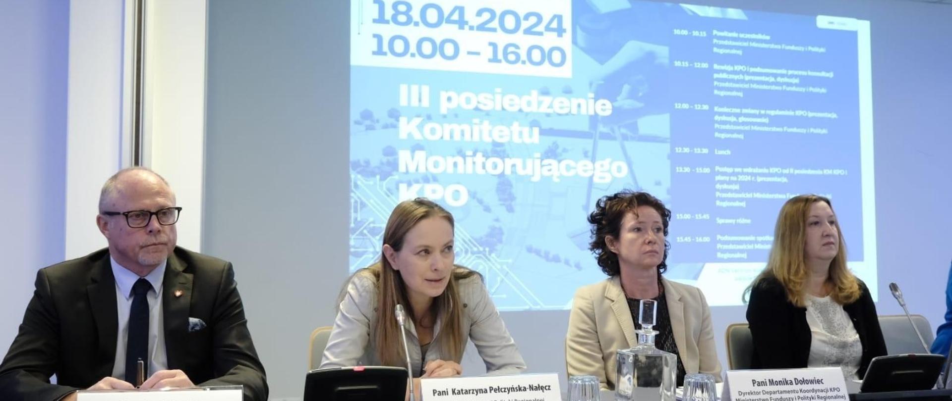 Cztery osoby siedzą obok siebie. Druga od lewej siedzi minister Katarzyna Pełczyńska-Nałęcz i patrzy przed siebie. Obok niej, pierwszy od lewej siedzi wiceminister Jacek Protas.