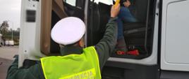 Umundurowany inspektor lubuskiej ITD stoi obok otwartych drzwi kabiny ciągnika siodłowego, trzyma w ręku alkomat przesiewowy i kontroluje trzeźwość kierowcy.