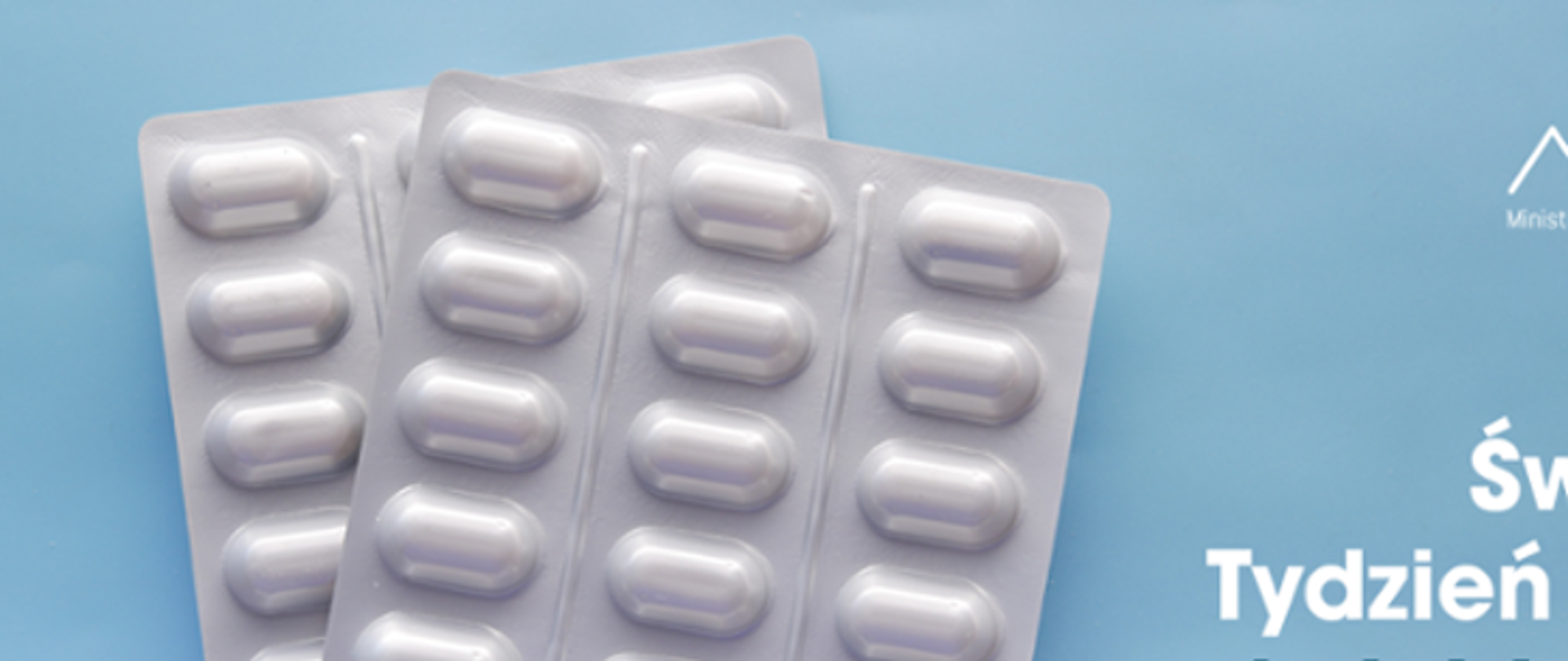 Na zdjęciu po lewej stronie znajduje się antybiotyk w postaci tabletek. Po prawej stronie widnieje logo Ministerstwa Zdrowia oraz Państwowej Inspekcji Sanitarnej. Poniżej widnieje napis Światowy Tydzień Wiedzy o Antybiotykach. Tło jest w odcieniu niebieskiego.