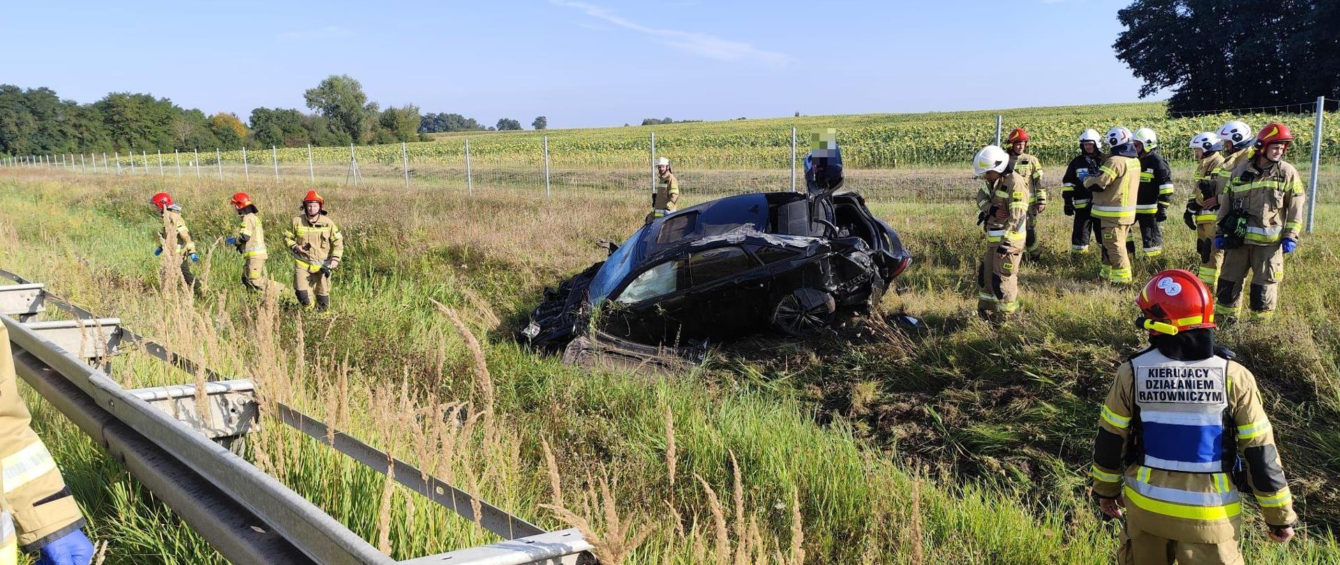 samochód po dachowaniu na poboczu wokół strażacy 