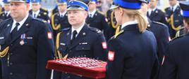 Wojewódzkie i Miejskie Obchody Dnia Strażaka - jednenvstrażak trzyma tacę z medalami, a obok stoją strażacy czekający na wręczenie