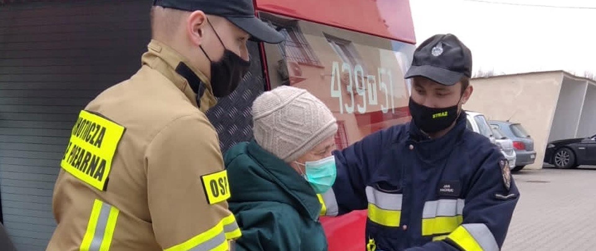Strażacy OSP Ruda Maleniecka pomagają wysiąść z samochodu strażackiego starszej pani