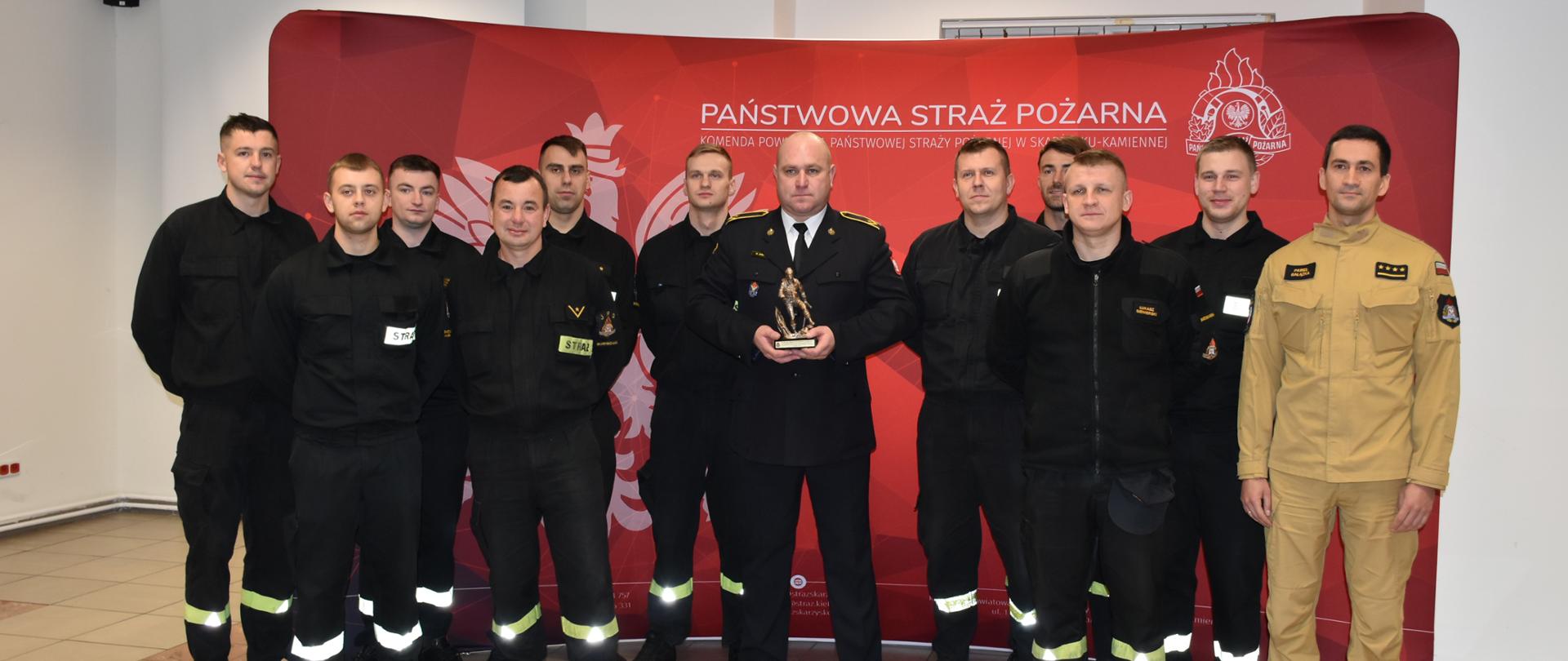 Zdjęcie strażaka odchodzącego na zaopatrzenie emerytalne. Trzyma on w rekach pamiątkową statuetkę.