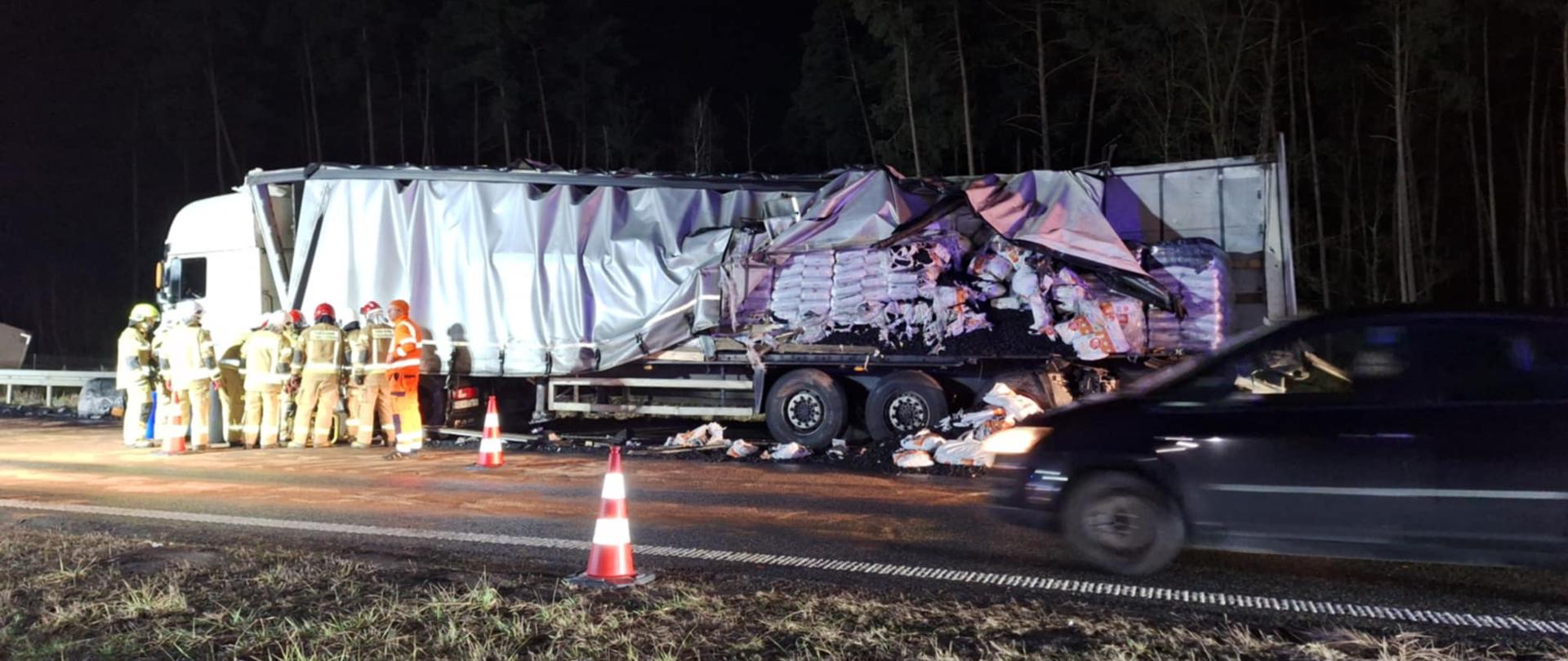 Droga ekspresowa S5. Na pasie awaryjnym stoi zestaw pojazdów: ciągnik siodłowy-naczepa, który uczestniczył w kolizji. Naczepa ma uszkodzona plandekę. Część przewożonego ładunku znajduje się na jezdni. Obok samochodu stoją strażacy, którzy przepompowują paliwo zuszkodzonego zbiornika samochodu do beczek.