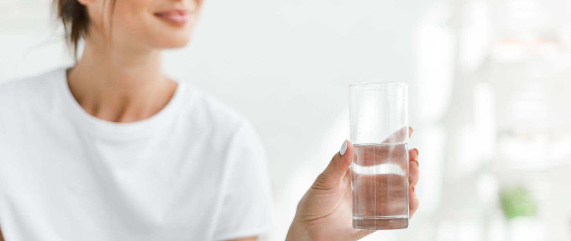 Na zdjęciu jest kobieta trzymająca szklankę z wodą.