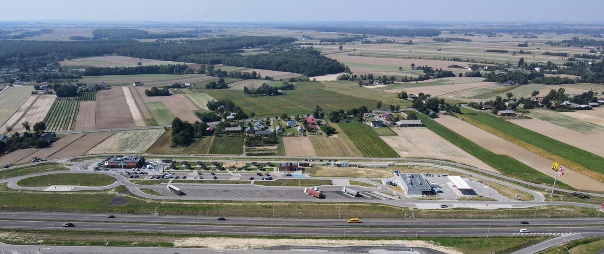 Zdjęcie z lotu ptaka na MOP Obroki przy drodze ekspresowej S19. Na jezdni widać ruch pojazdów. Na MOP zaparkowane auta, świeżo udostępniana stacja paliw i restauracja.