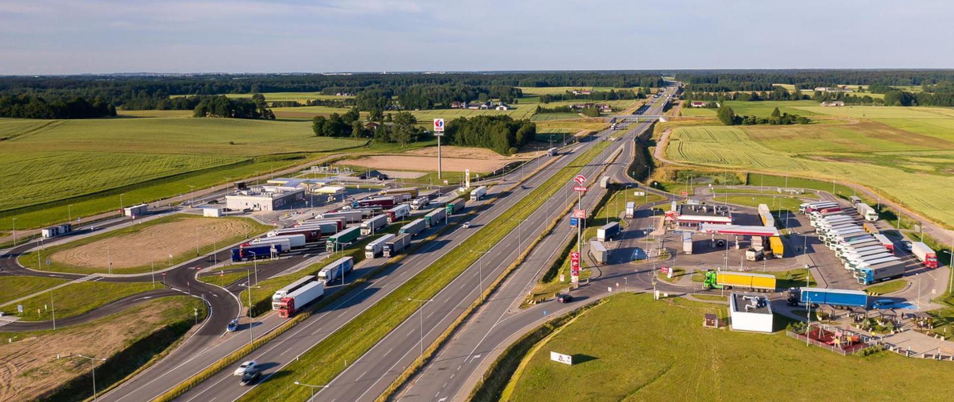 Miejsce Obsługi Podróżnych - po obu stronach dwujezdniowej drogi ekspresowej parkingi ze stacjami paliw. Zaparkowane samochody ciężarowe. Ujęcie z lotu ptaka 