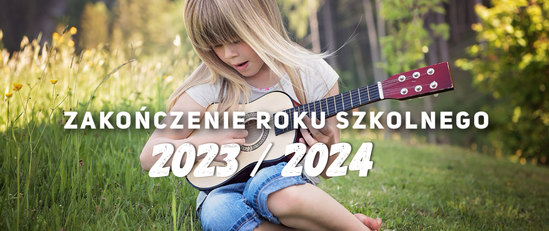 Na zdjęcie znajduję się dziewczynka grająca na ukulele. Siedzi na zielonej trawie. 