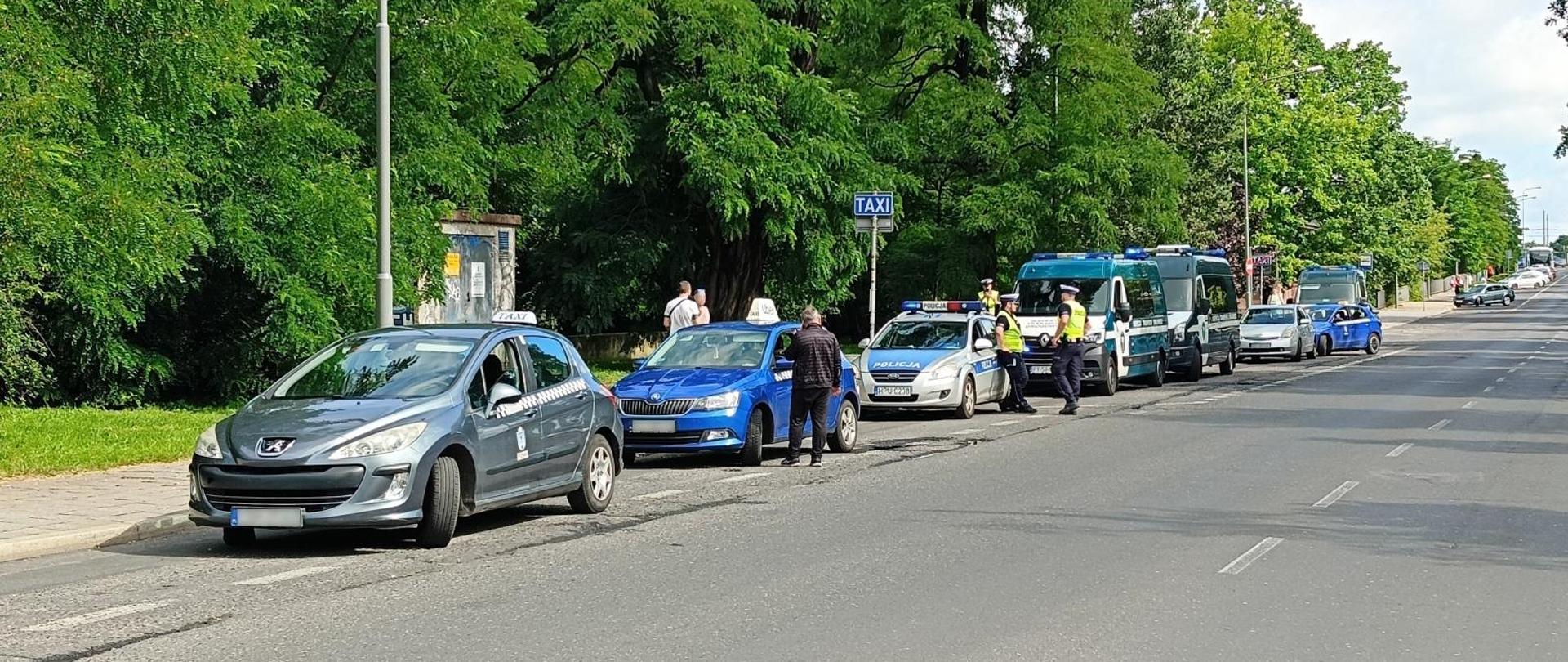 Szereg samochodów podczas kontroli taksówkarzy, w tym samochód policji oraz Inspekcji Transportu Drogowego.