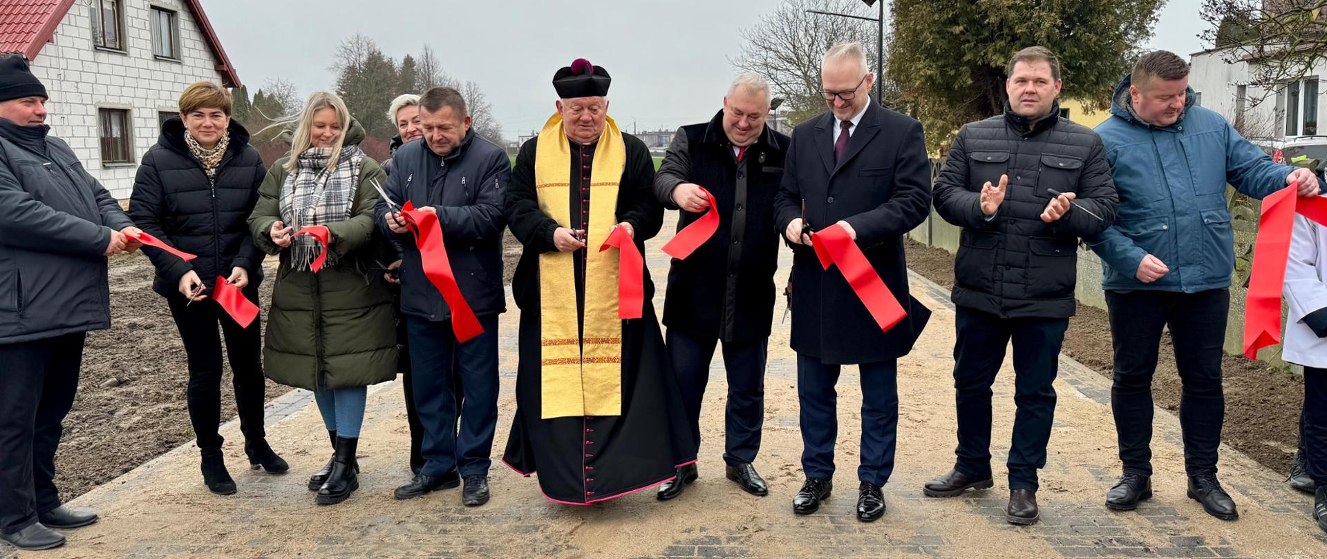 Uroczyste otwarcie ciągu pieszo-jezdnego w Płośnicy w dniu 30 grudnia 2024 r. - zebrani w miejscowości Płośnica stoją na drodze w dobrych nastrojach.