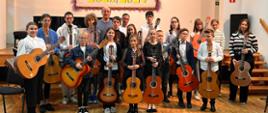 Zdjęcie grupowe przedstawiające wszystkich wykonawców popisu klasy gitary w auli szkoły w dniu 26 października 2023 roku.