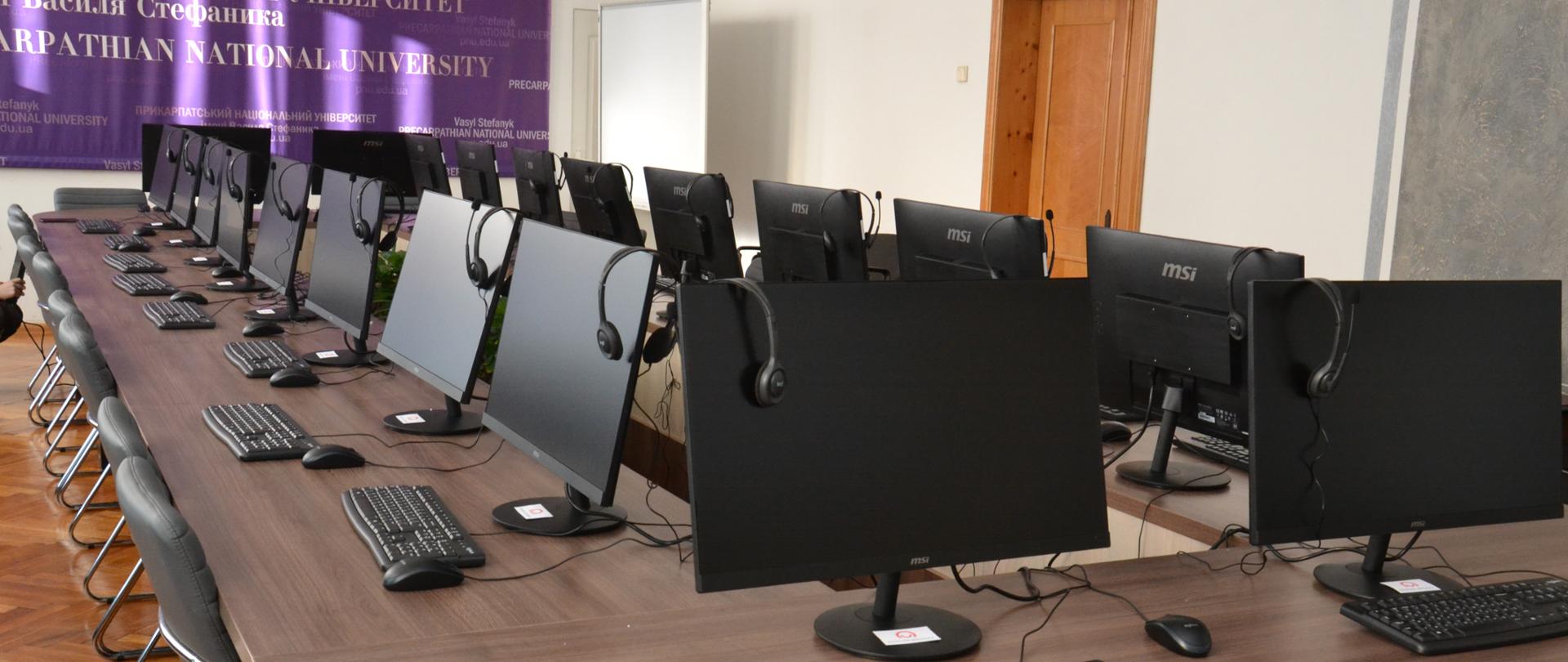 Sala komputerowa z licznymi stanowiskami komputerowymi.