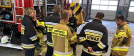 na zdjęciu widoczni strażacy na garażu jednostki w trakcie egzaminu ze znajomości sprzętu, w tle samochód pożarniczy