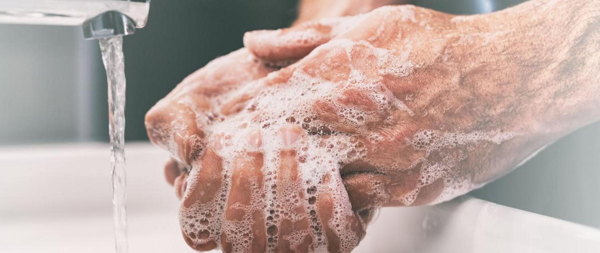 Osoba myjąca ręce mydłem i wodą lecącą z kranu