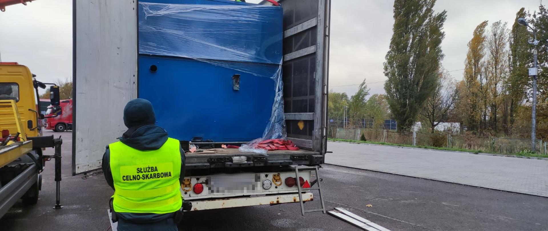 Funkcjonariusz Służby Celno-Skarbowej z tyłu samochodu ciężarowego, otwarta naczepa.