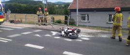 Motocykl na jezdni a obok strażacy
