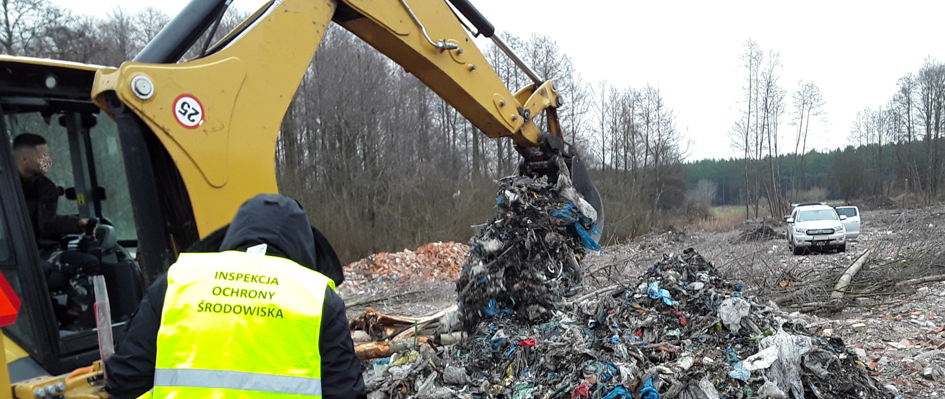 Inspektor Wojewódzkiego Inspektoratu Ochrony Środowiska w Warszawie stoi przy koparce przekopującej nielegalnie zgromadzone odpady.
