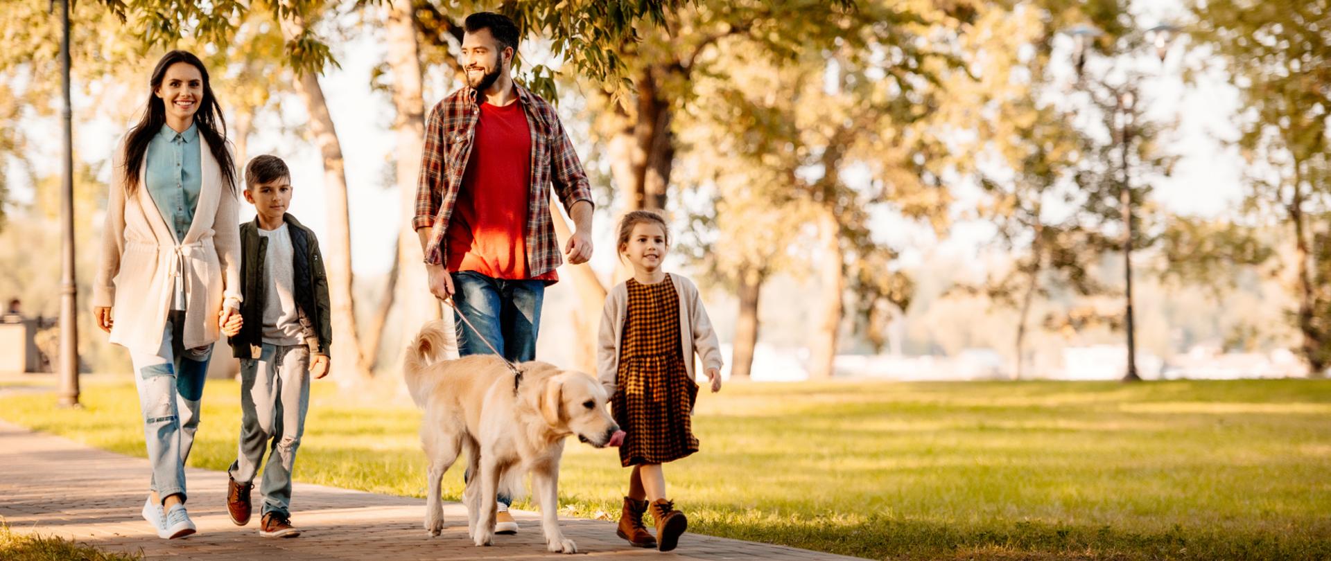 Na zdjęciu jest rodzina - mama, tata, brat i siostra. Tata prowadzi psa. Rodzina znajduje się w parku.