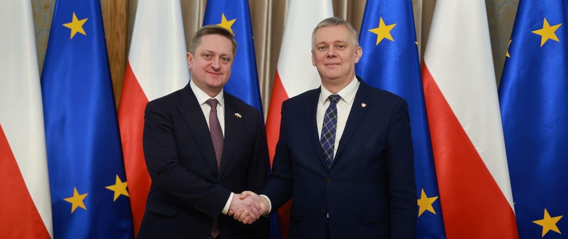 Minister_Koordynator Służb Specjalnych z Ambasadorem Ukrainy wymieniają uścisk dłoni na tle flag Polski i Unii Europejskiej
