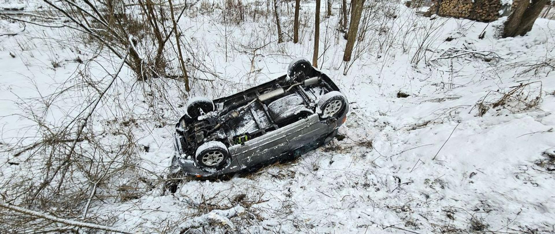 Samochód osobowy lezy na dachu poza drogą