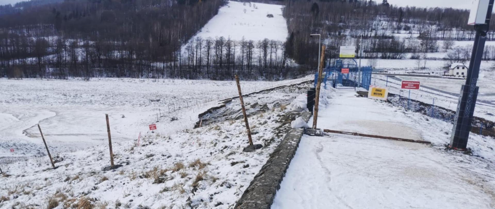 Wygrodzenie i oznakowanie tablicami ostrzegawczymi strefy niebezpiecznej w odległości 10 m od krawędzi zniszczonej lewej skarpy zapory od strony odwodnej i odpowietrznej oraz prawej skarpy zapory od strony odwodnej i odpowietrznej w odległości 15 m od budowli kamiennej zapory czołowej.