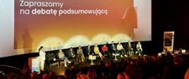 Debata podsumowująca Kongres Efektywnej Komunikacji - pod dużym ekranem siedzi kilkanaście osób, które prowadziły dyskusje i warsztaty podczas Kongresu