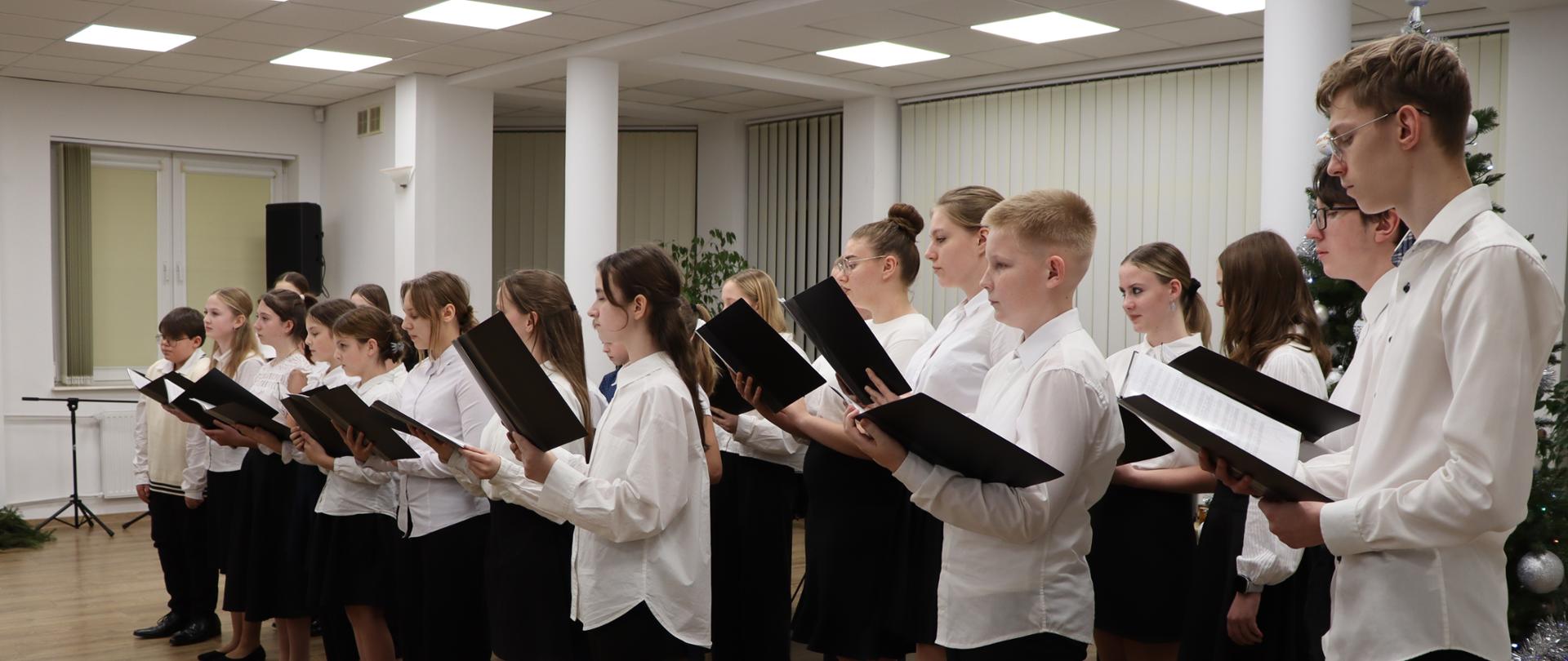 Koncert kolęd. Chór szkoły muzycznej stoi w sali koncertowej i śpiewa. 