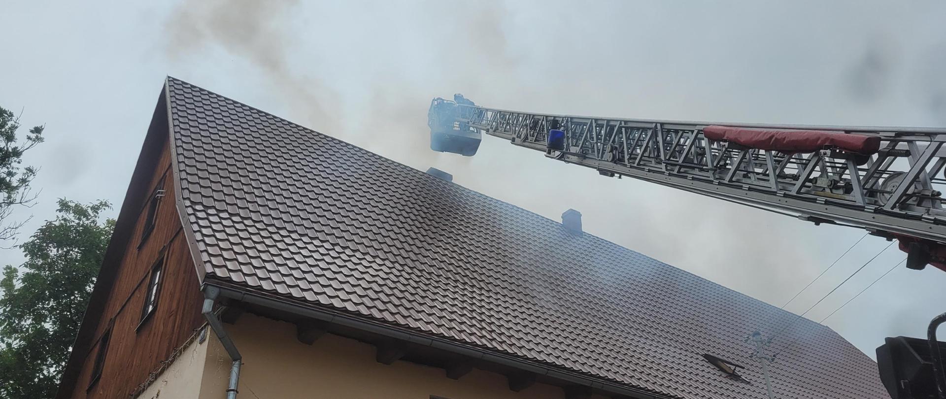 Budynek jednorodzinny, ze strażackiej drabiny mechanicznej strażacy gaszą pożar komina, dużo dymu