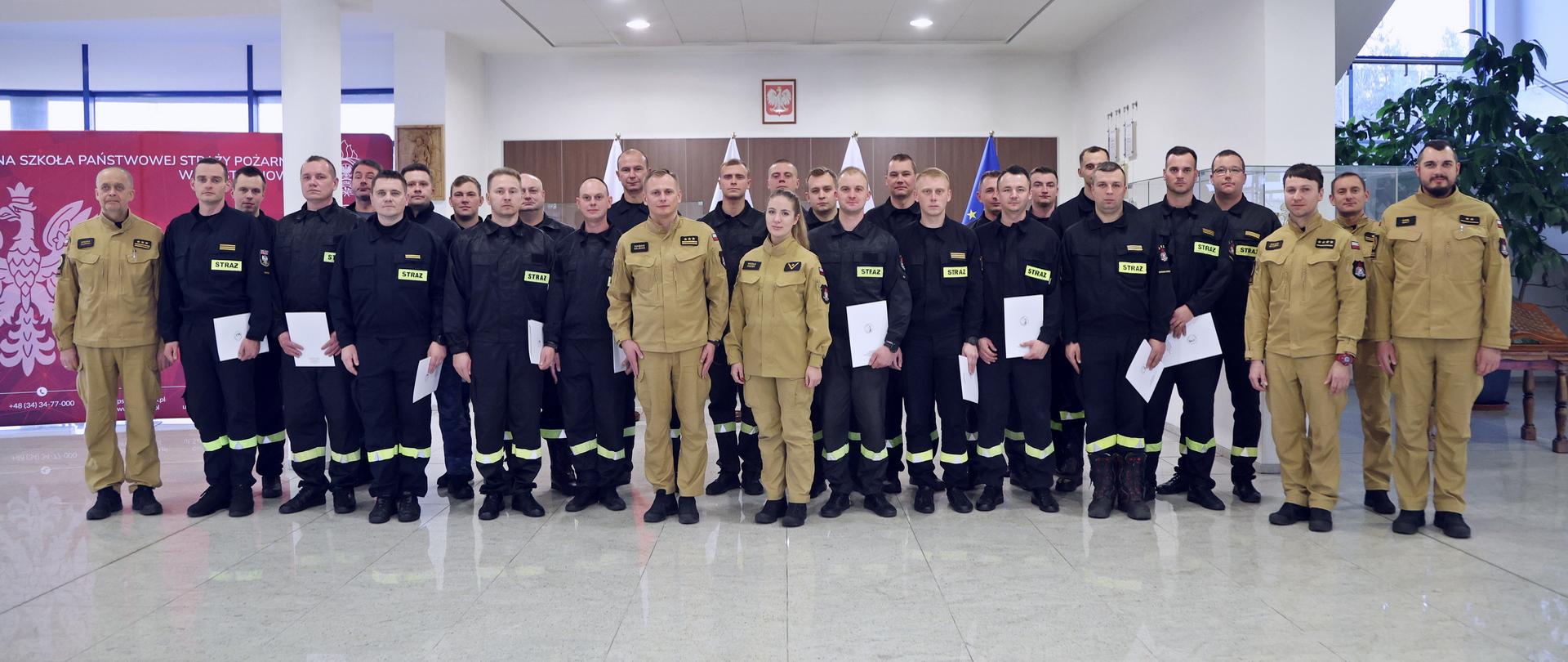 Pamiątkowe zdjęcie grupowe funkcjonariusze PSP będących uczestnikami szkolenia ratownictwa chemicznego i ekologicznego (24 osoby) w towarzystwie Zastępcy Komendanta Centralnej Szkoły PSP, czterech funkcjonariuszy CS PSP oraz funkcjonariuszki CS PSP