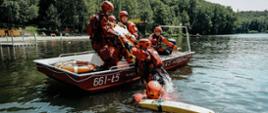 Strażacy na łodzi wyjmują innego strażaka z wody na pokład podczas ćwiczeń