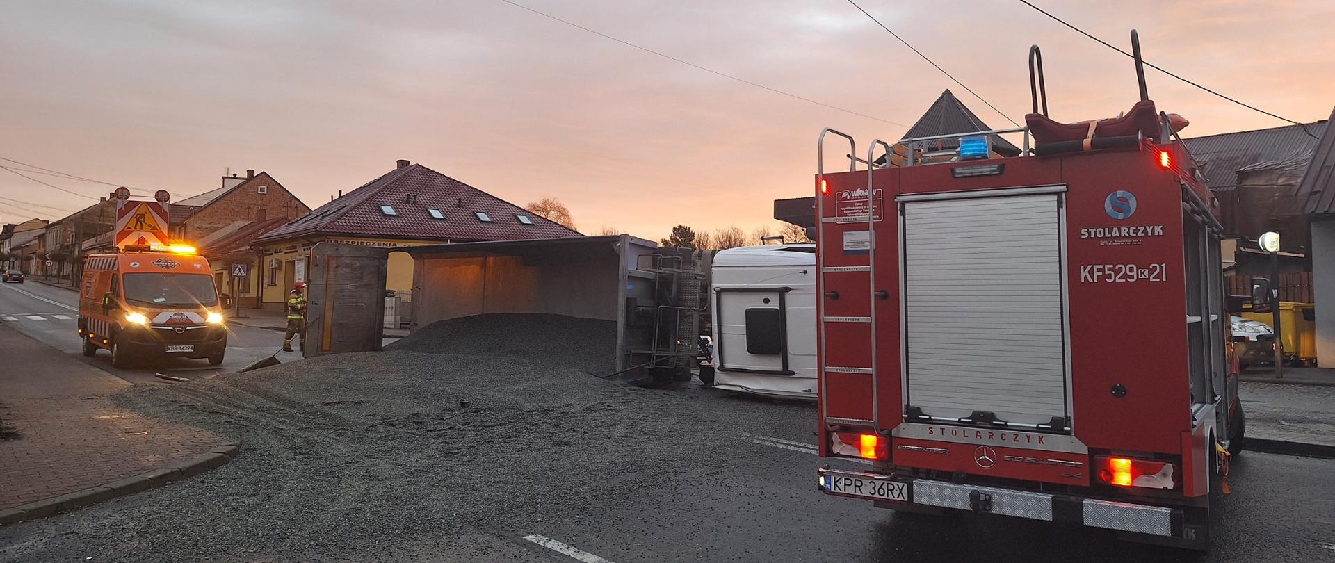 Wypadek samochodu ciężarowego - pojazd leży na prawym boku obok samochód strażacki