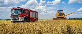 Na zdjęciu rolnik podczas zbioru ziarna na polu oraz w tle czerwony samochód Straży Pożarnej.