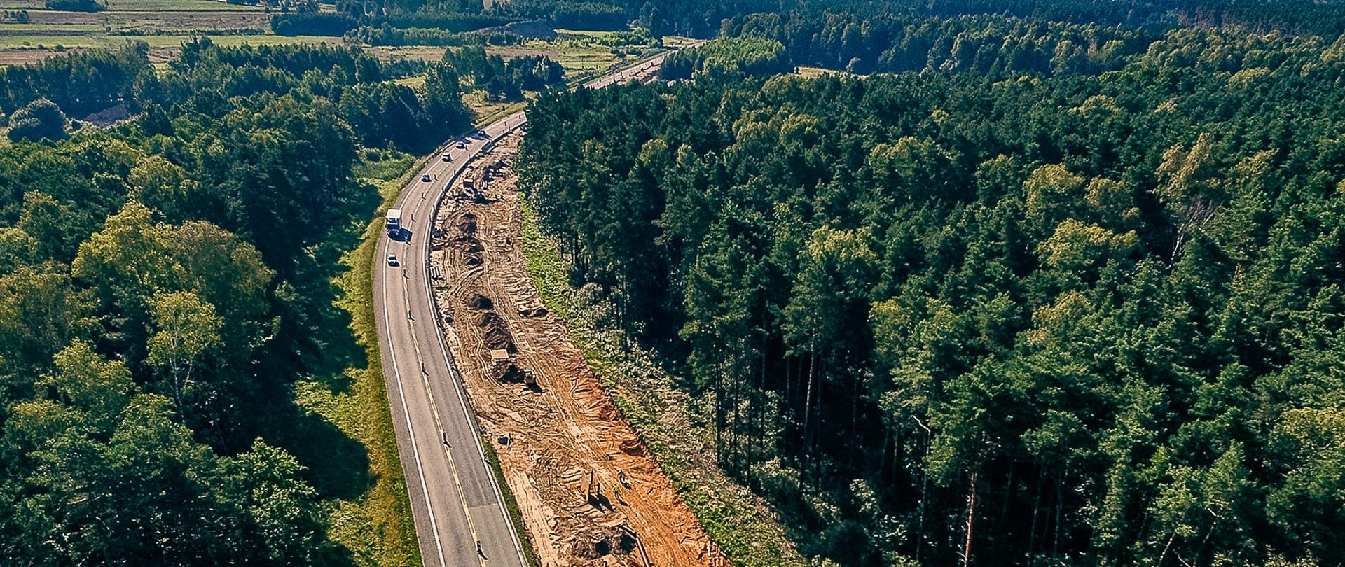 Poprawa bezpieczeństwa ruchu drogowego na sieci TEN-T na drodze krajowej nr 91 (dawniej nr 1) - przebudowa odcinka Markowice – Brudzowice. Na zdjęciu prace budowlane, po obu stronach drogi i w tle widoczny las.