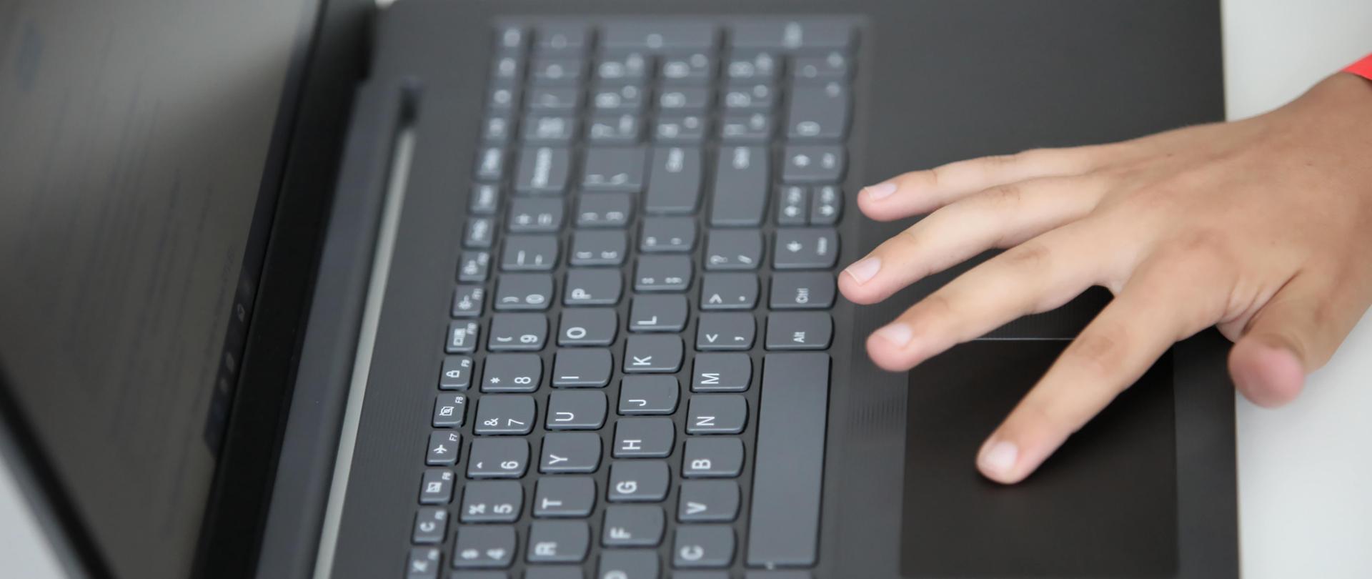 Laptop z dłonią na touchpadzie - fot. Leszek Szymański