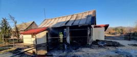 Zdjęcie przedstawia budynek garażu, który uległ spaleniu, Wewnątrz widać strażaków. Garaż został wygrodzony taśmą. 