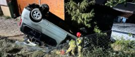 Fotografia przedstawia strażaków pracujących przy pojeździe osobowym typu Van. Pojazd leży na dachu poniżej skarpy, widać zniszczone ogrodzenie z siatki, jest ciemno.