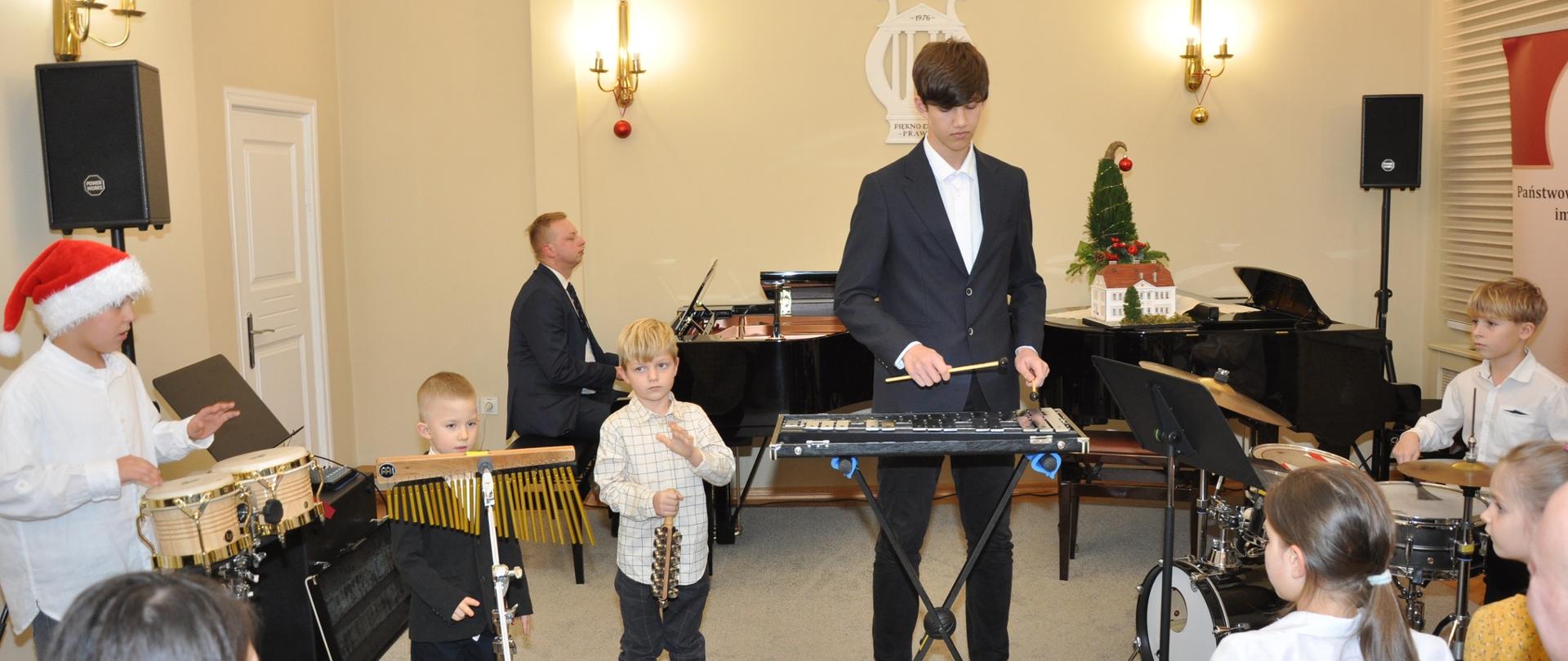 Występ zespołu perkusyjnego podczas koncertu świątecznego w auli szkoły. W tle przy fortepianie akompaniuje p. Szymon Franek.