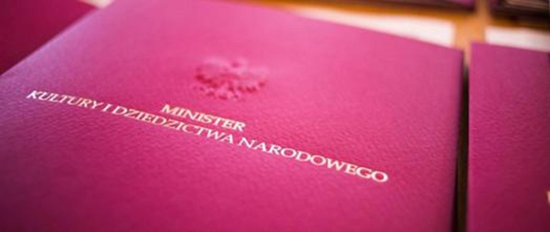Zdjęcie papierowej teczki aktowej w kolorze bordowym z wypukłym orzełkiem z napisami drukowanymi literami Minister Kultury i Dziedzictwa Narodowego
