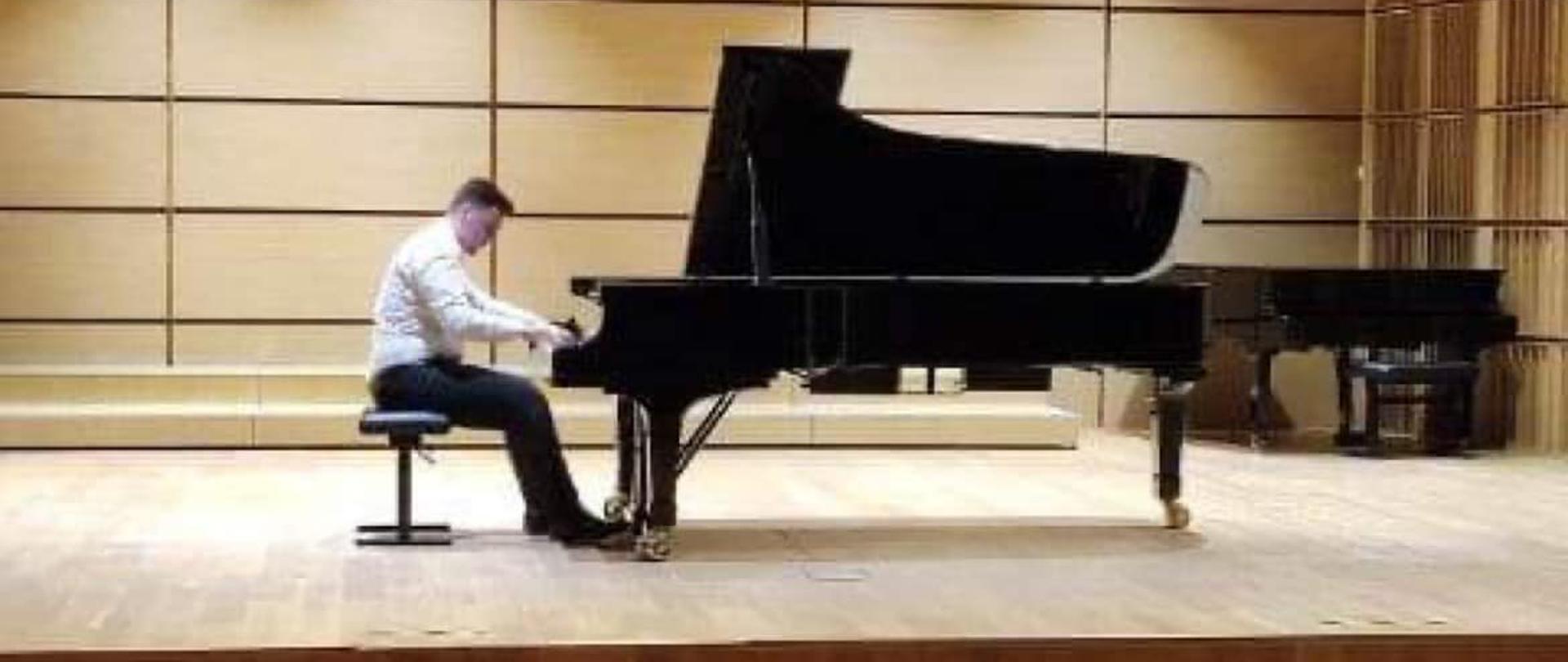 Pianista grający na fortepianie na sali koncertowej. Z tyłu, po prawej stronie widoczny drugi fortepian. Na dole widownia.