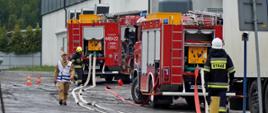Na zdjęciu widoczne czerwone samochody pożarnicze oraz strażacy podczas rozwijania węży strażackich w trakcie powiatowych ćwiczeniach taktyczno-bojowe pod kryptonimem „Empol 2023” 