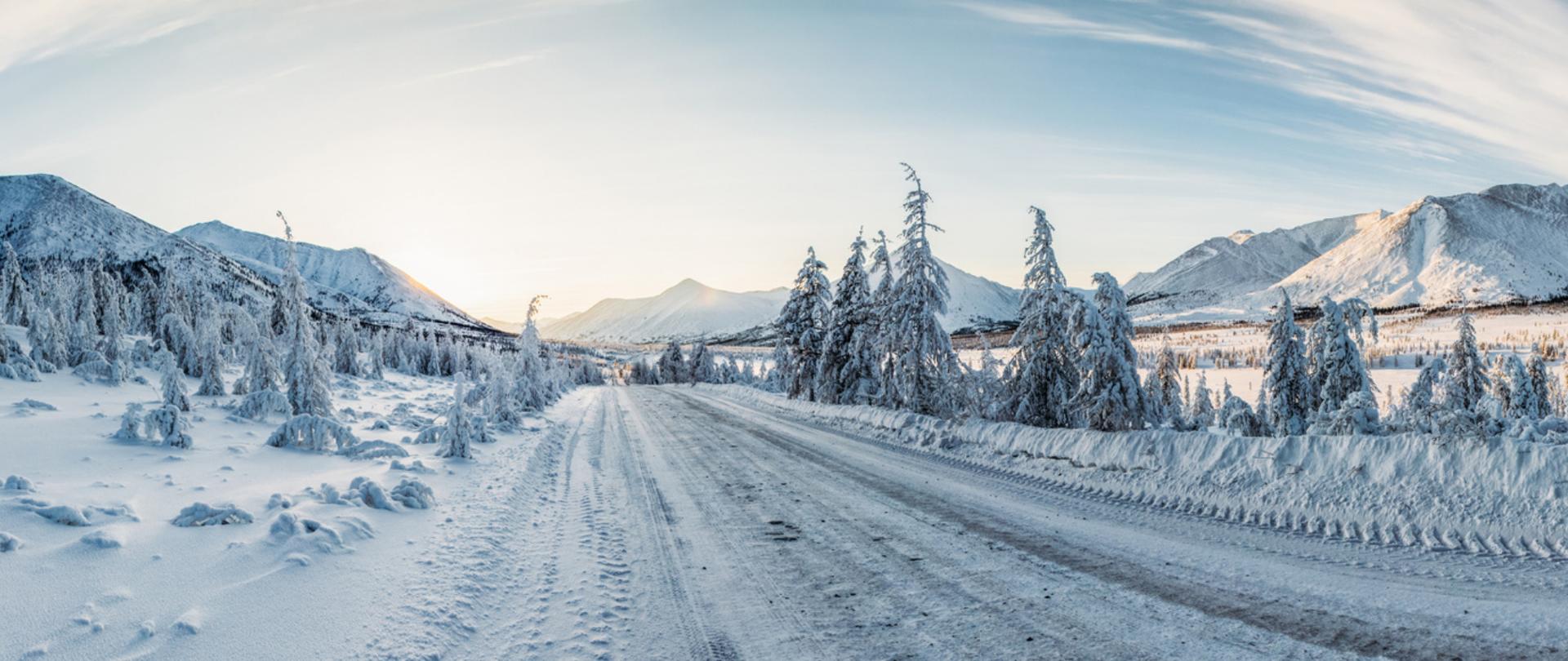 Na zdjęciu jest ukazany krajobraz zimowy - zaśnieżona droga, drzewa i góry.
