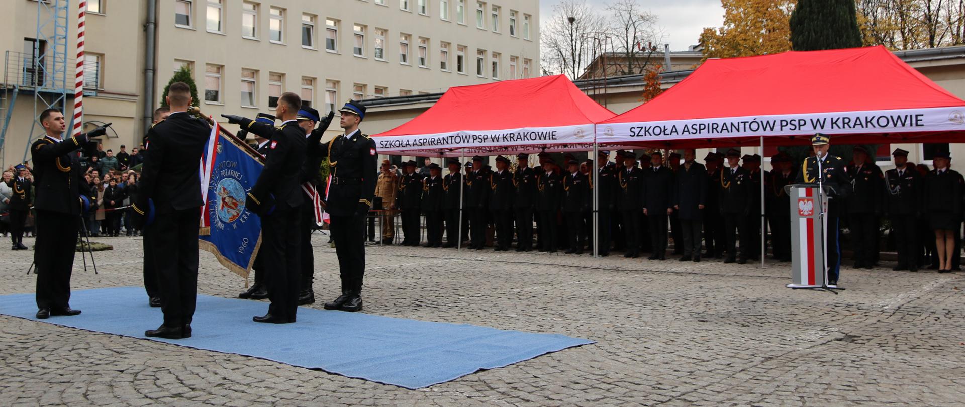 Ślubowanie na sztandar. Czterech słuchaczy składa rotę ślubowania. Mężczyźni – strażacy – w umundurowaniu wyjściowym. 