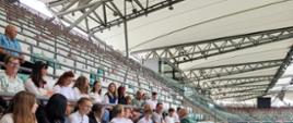 na trybunach stadionu siedzi grupka uczniów słucha wypowiedzi pracownika stadionu.