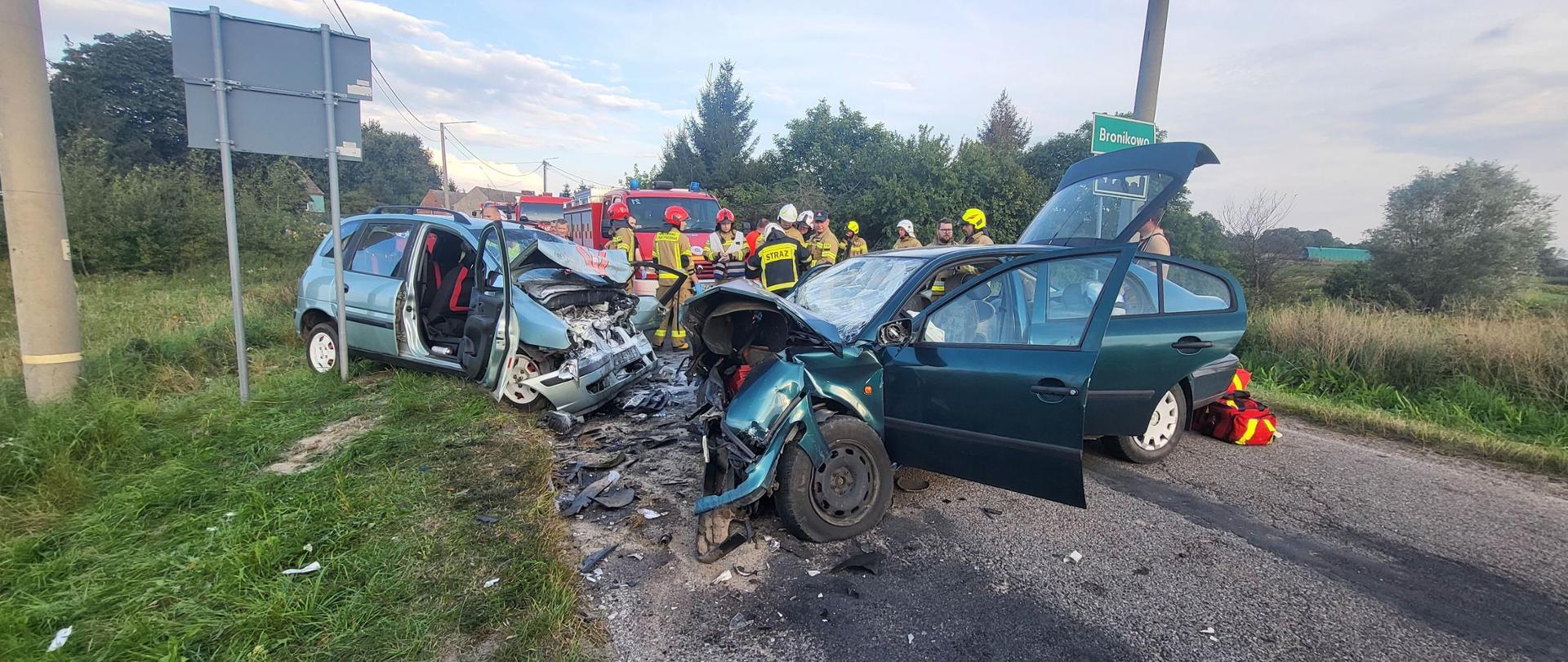 Wypadek drogowy na drodze wojewódzkiej w Bronikowie, na pierwszym planie uszkodzone 2 auta na drodze asfaltowej